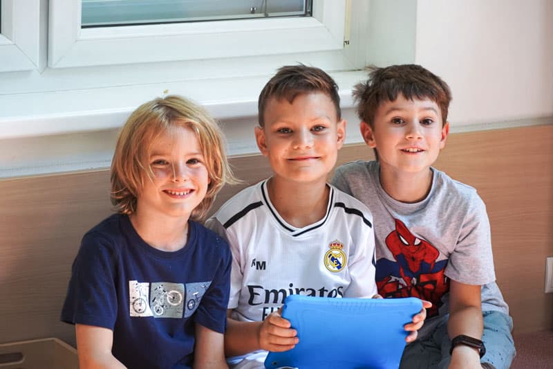 3 Burschen im Alter von ca. 10 bis 11 Jahren nehmen an einem Herbstferien Camp von Robomaniac teil, sie haben ein blaues Tablet für Robotik Programmierung in der Hand